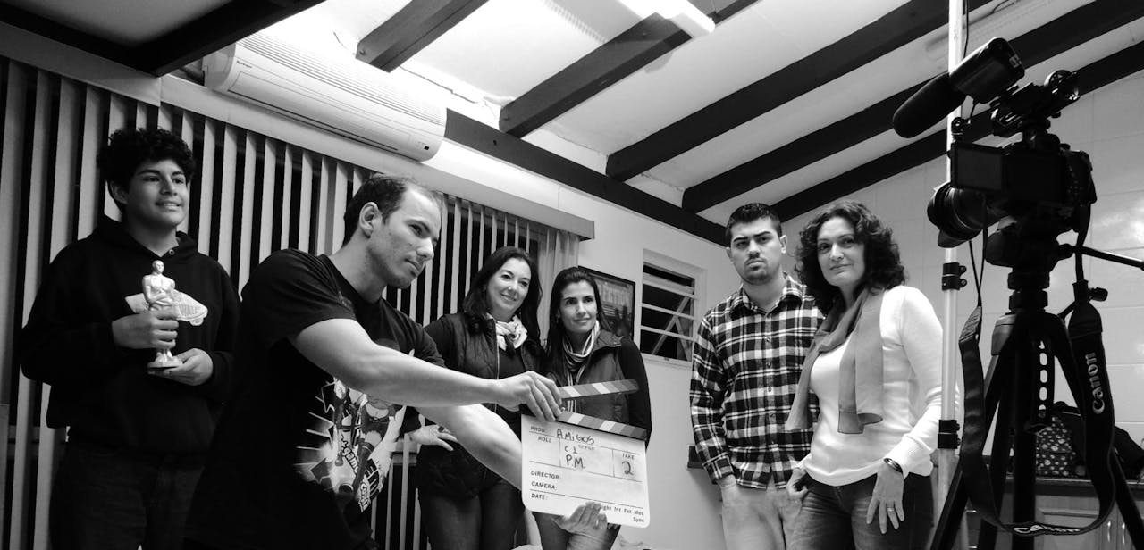 about-02 A group of adults collaborate on a filmmaking project, seen holding a clapperboard indoors.
